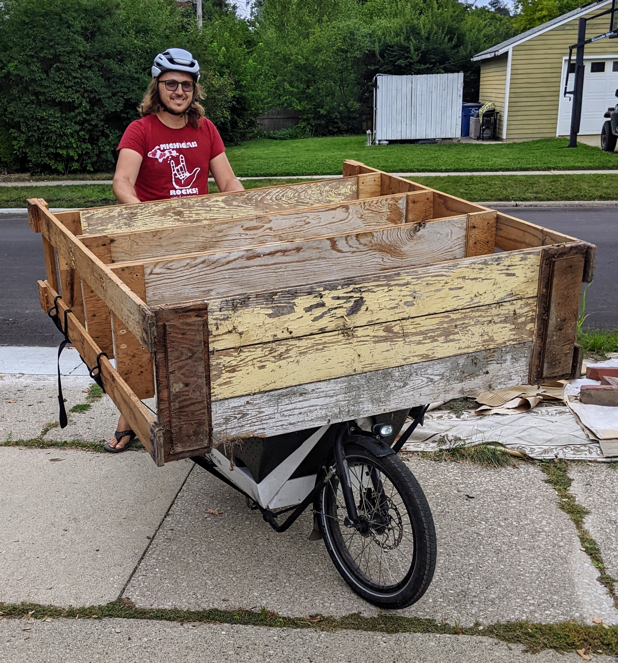 Joe on a cargo bike with a box in front. Strapped on top of the bike is a shelving unit.